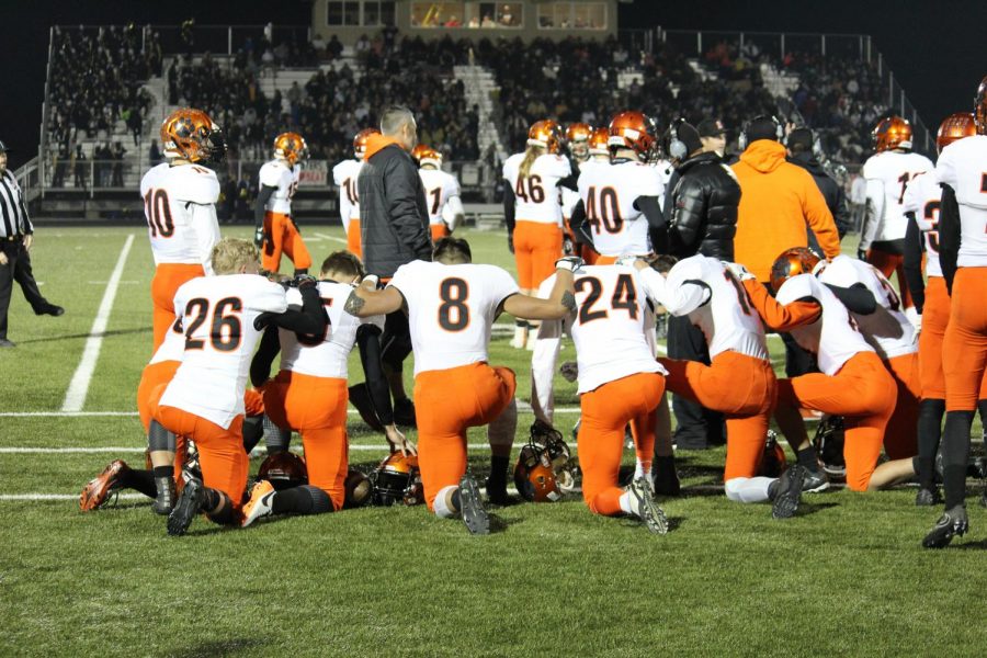 From right to left: Mason Veve (26), Noah Roper (8), Alex Mathis (24) and others pray before kickoff